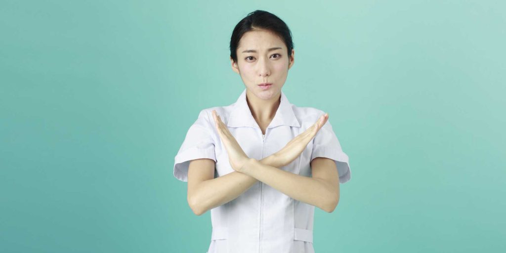 バツ印を出している女性看護師の画像